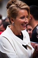 Upper torso of a blond-haired woman who is wearing a white coat over a black shirt.