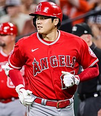 Shohei Ohtani wearing red Los Angeles Angels uniform, jogging towards the camera and facing off to the left.