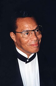 1997 photo of Farrakhan, the leader of the NoI. He is staring to the right, away from the camera, and wearing a suit.