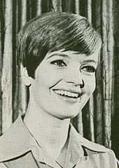 A woman in her thirties with short, parted hair in a black-and-white portrait shot. She wears a khaki shirt.