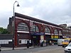 A red-bricked building with a rectangular, white sign reading "KENTISH TOWN STATION" in black letters all under a light blue sky