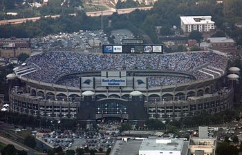 Aerial shot of an open air stadium during a football game. The outside facing is defined by a series of arches, and scoreboards are visible at the top of the facility.