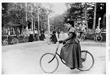 The Canadian photographer Hannah Maynard is seen cycling in Beacon Hill park in 1892, with many more cyclists relaxing against a stone wall with their bicycles in the background.