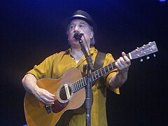 Paul Simon sings live with a guitar in hand.