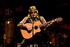 A man is sitting on a stool playing a guitar.