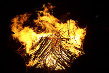 A night-time photograph of a blazing fire is silhouetted by dark figures.