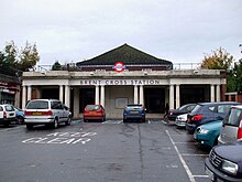 A two-storey station building with a wide colonnaded entrance beneath a peaked roof.