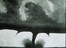 Three dark funnels silhouetted against a grey background beneath swirling clouds