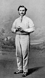 A cricketer holding a ball posing before a painted backdrop of a field