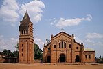 Photograph depicting the Catholic parish church in Rwamagana, Eastern Province, including the main entrance, facade, the separate bell tower and dirt forecourt