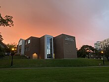 A brick building with many windows and text that reads "Conrad Grebel University College", with a pink sunset in the background