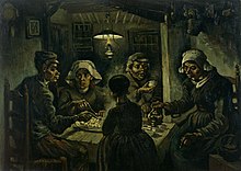 A group of five sit around a small wooden table with a large platter of food, while one person pours drinks from a kettle in a dark room with an overhead lantern.