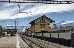 Island platform with a shelter; there is three-story building with gabled roof at left