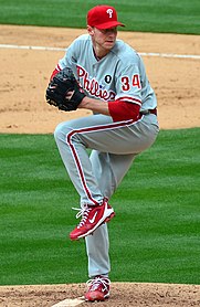 Photograph of Roy Halliday wearing the Phillies' grey road uniform with red lettering/numbering and a "Whip" Buck patch