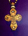 A golden cross decorated with four large gems, depicting Jesus