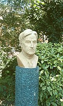 Outdoor bust of middle aged man with good head of hair, against a garden background