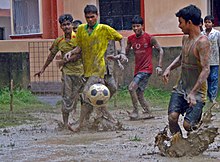 several young men playing association football in a muddy field in the rain