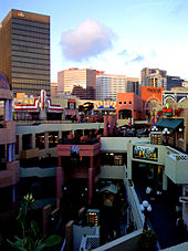 Several buildings in front with signs for various stores, high skyscraper behind them on left with NBC logo