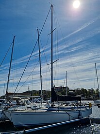 A mostly white boat of the type Swan 371 docked in Kristiansand, Norway. The sails are not raised, and there are other ships in the background.