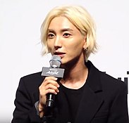 Leeteuk speaking into a microphone and looking slightly to the left