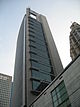 Ground-level view of a 30-storey building with a rounded, glass facade on one side and a straight-edged facade of concrete and windows on another; the concrete siding protrudes above the roofline