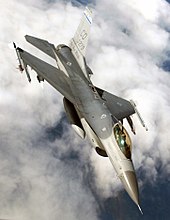 Upright aerial photo of gray jet aircraft flying above clouds.