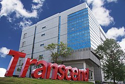 A view looking upward at a gray office building, with the Transcend logo in the grass in front