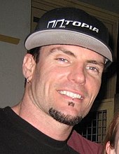 Head shot of Vanilla Ice with a goatee wearing a black t-shirt and baseball cap.