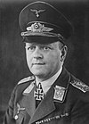 A man wearing a peaked cap and military uniform with various military decorations including an Iron Cross displayed at the front of his uniform collar.