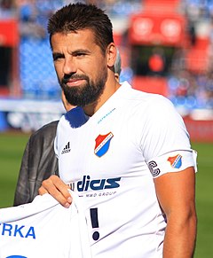 Photograph of a player in a white football kit standing on grass