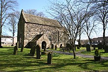 A small plain church building with a stone porch and no tower. The church is surrounded by a graveyard and trees without leaves.