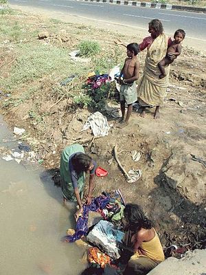 Women washing clothes in ditch alongside main road in Mumbai