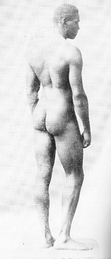 a naked white man standing with his back to the camera and his face in profile