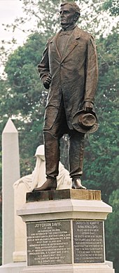 standing statue of man in 1800 suit looking left, both hands down, right hand is holding a brimmed hat