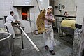 Inside the bakery; one person bakes and another removes bread from the oven.