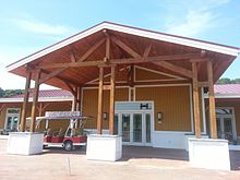 A large wooden building with a red roof, three wooden posts, with an electric golf cart parked in front.