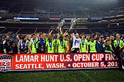 Several players are standing together lifting two large trophies upward