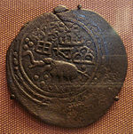 An old coin with a offcenter stamped design showing an elephant and geometric designs or writing