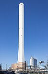 Ground-level view of a tall, white, angular chimney rising from a brown, striped building