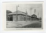 black and white photo of large rail station with streetlight, utility poles, and parked trolley cars