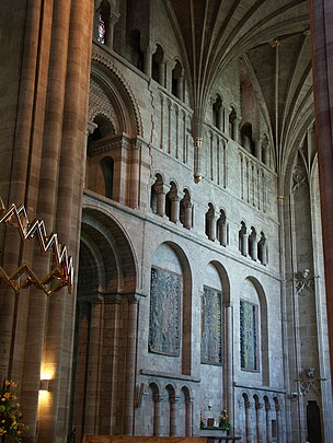 A transept interior with a wall panelled with shallow Norman arches and open galleries.