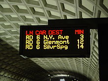 An electronic sign with multicolor text display mounted over a station platform.