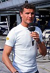 David Coulthard holding a microphone in his left hand speaking to the British media