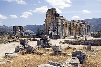 Exterior view of a ruined colonnaded building of which one wall still stands