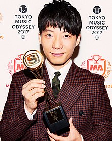 Hoshino at the 2017 Space Shower Music Awards, wearing a suit and holding the award for Best Video of the Year for "Koi"