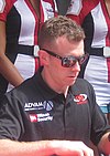 A man in his early thirties wearing black rectangular sunglasses and a black T-shirt