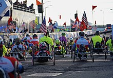 Multiple competitors in a mixture of high and low stance handcycles, all facing away from the camera.