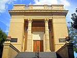 The stairs and front entrance to an impressive Renessaince Revial era institutional building, with brass plaques on both sides of the portico.