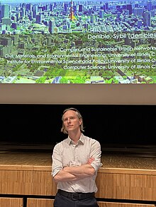 Sybil Derrible standing, with a projected slide behind him