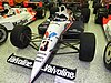 A black and white racing car adorned with sponsors logos and the number 3 in black on the front wing sitting in a museum